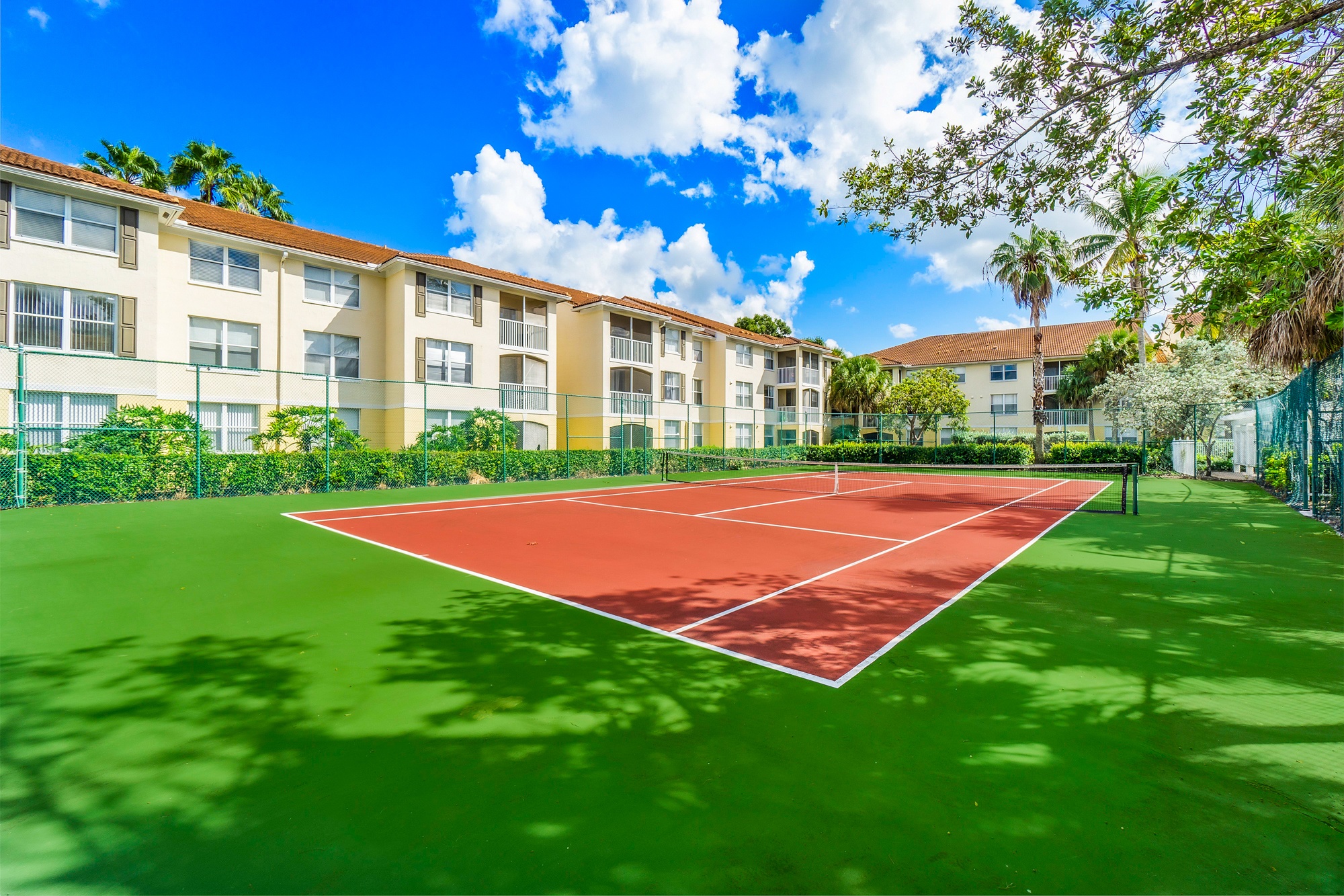 A tennis court is surrounded by apartment buildings.